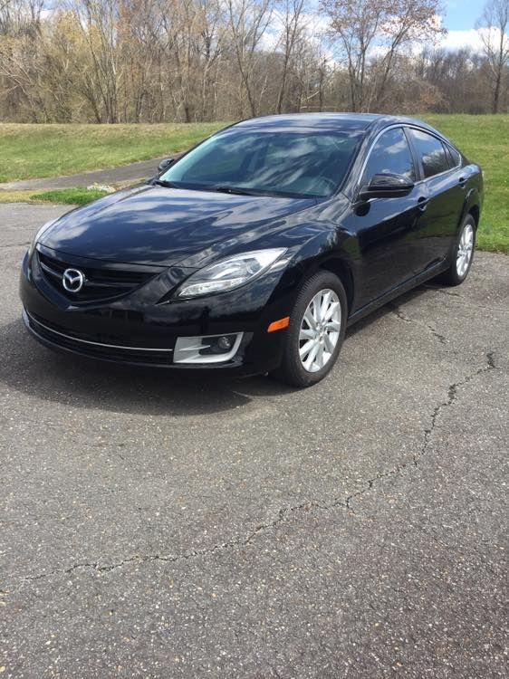 Black Mazda 6 sedan parked on asphalt. Outdoors with trees in the background.