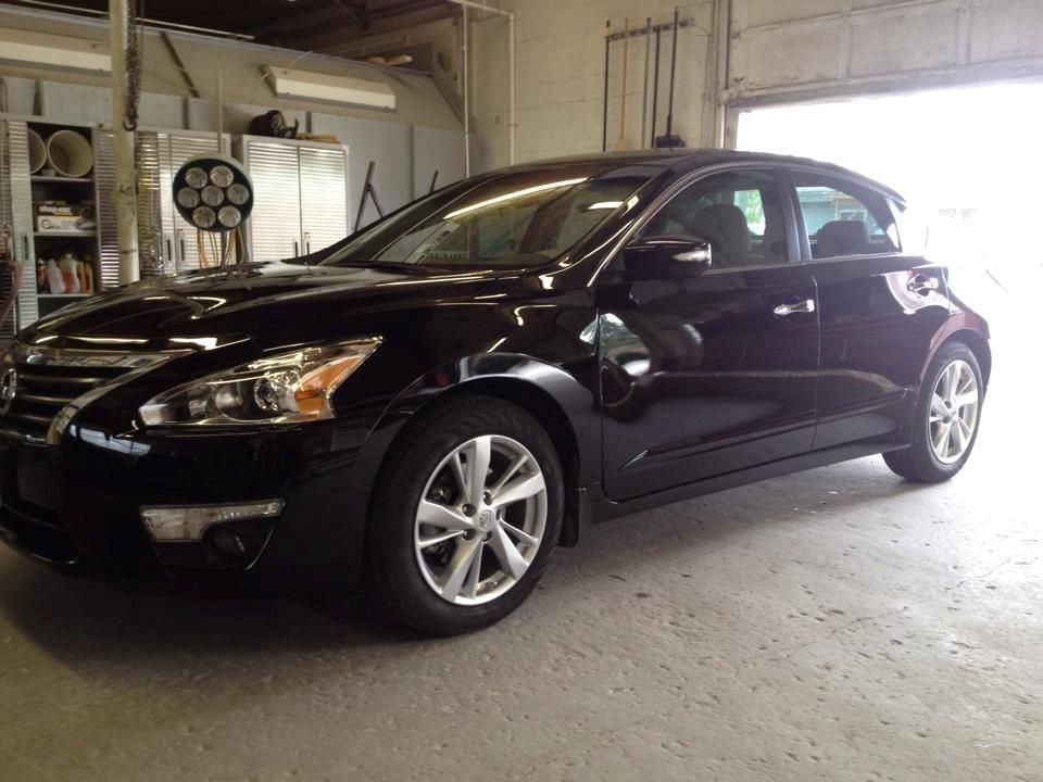 Black Nissan Altima in a garage, facing right, with open door in background.