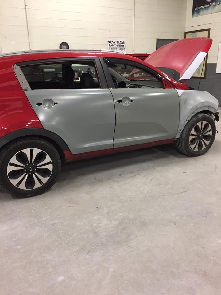 Red and gray Kia Sportage car in a garage with open hood and body panels removed.