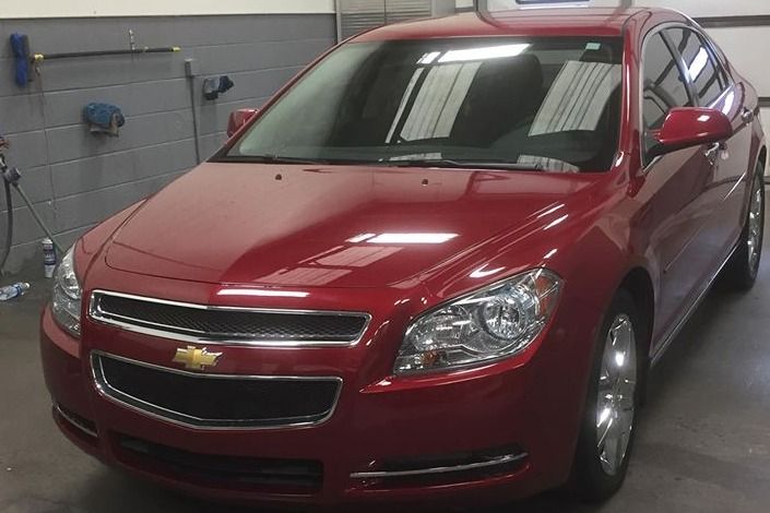 Red Chevrolet Malibu sedan parked inside a garage, with a shiny exterior finish.