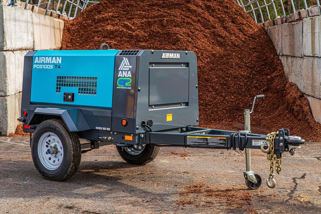 A small air compressor on a trailer is parked in front of a pile of mulch.