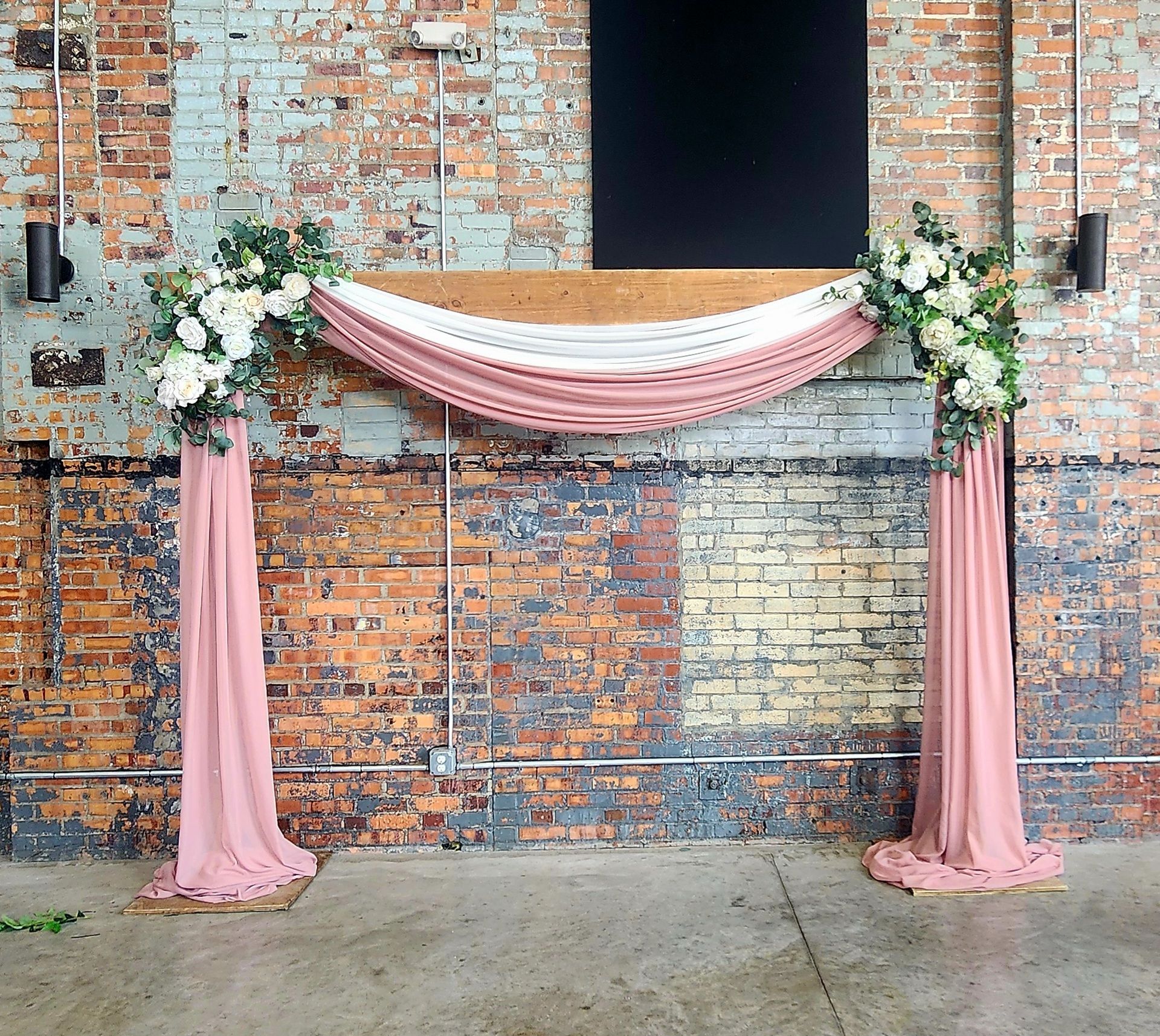 A brick wall with a pink and white arch decorated with flowers.