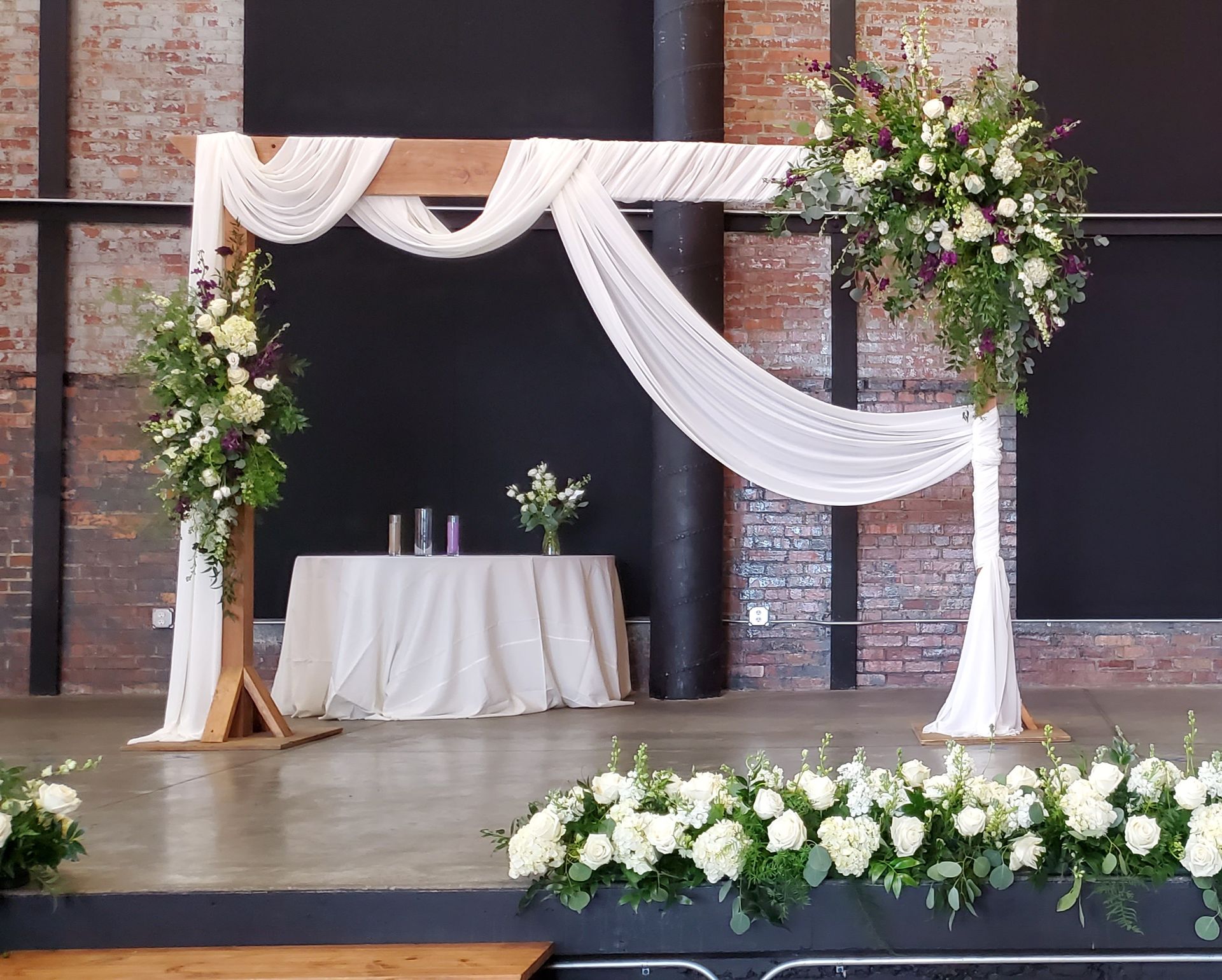 A wooden arch decorated with white cloth and flowers