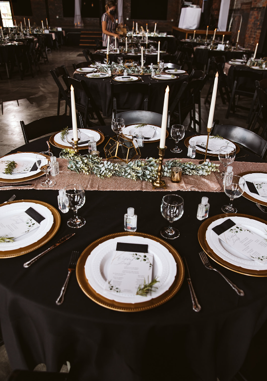 A table set for a wedding reception with plates , candles , and silverware.