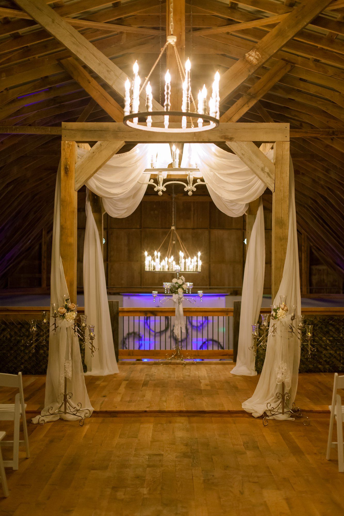 A wedding ceremony is taking place in a barn with a wooden arch and a chandelier.
