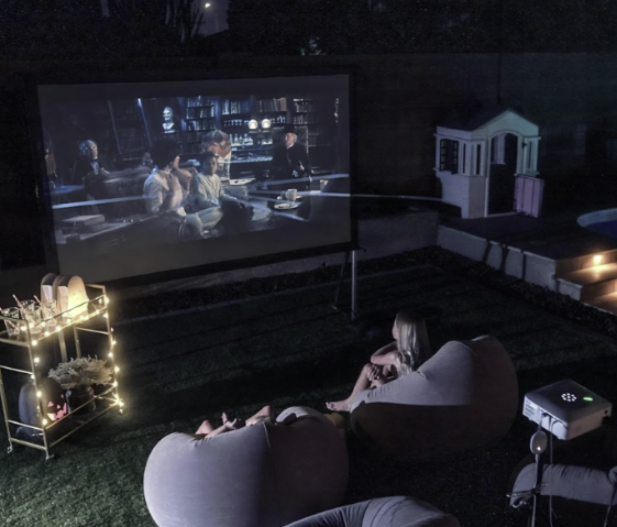 A woman sits in a chair watching a movie on a large screen