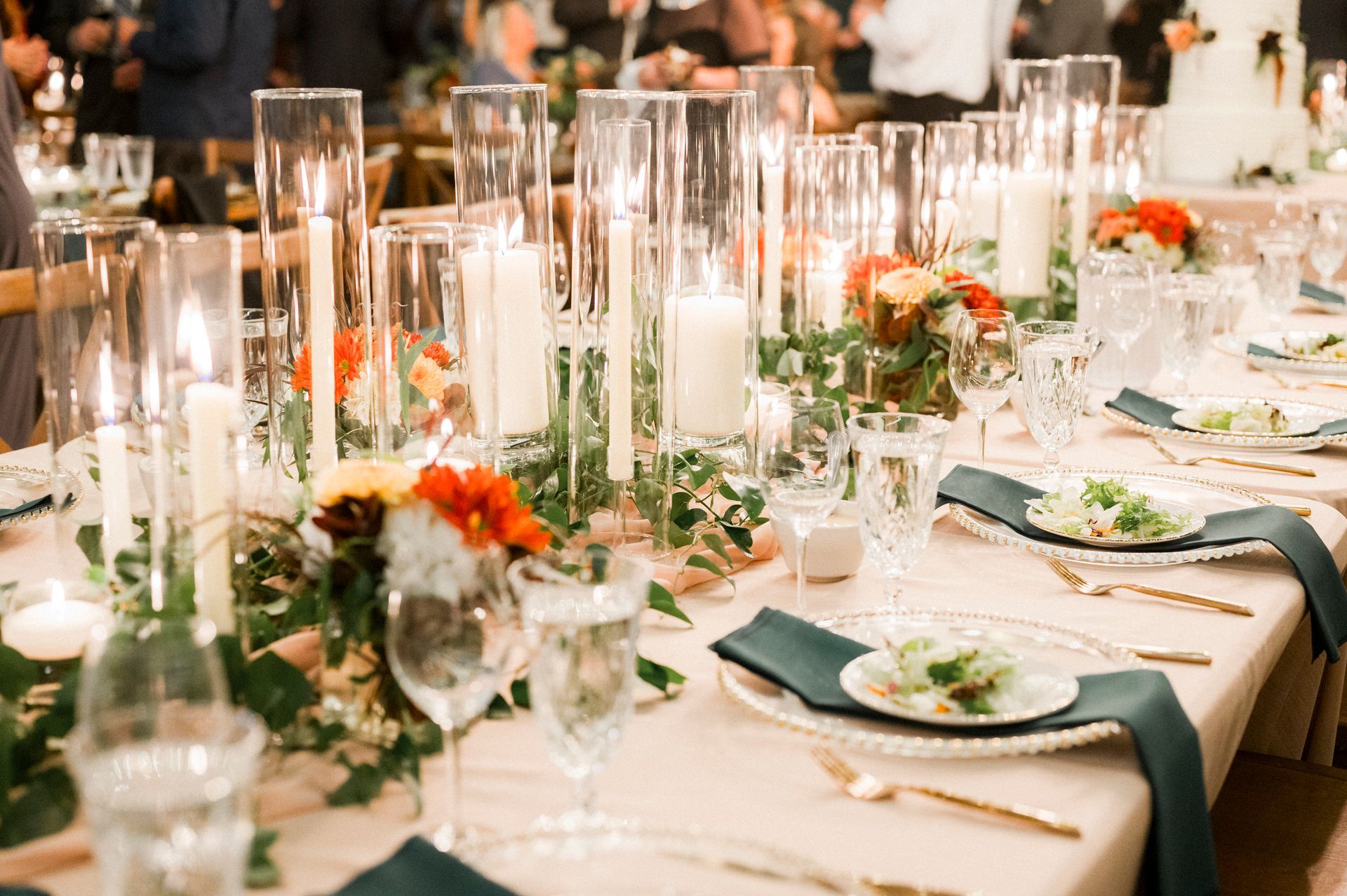 A long table set for a wedding reception with plates , glasses , candles and flowers.