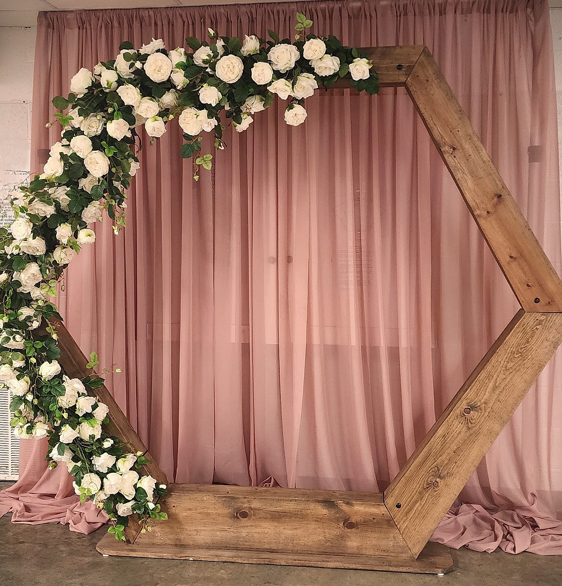 A wooden arch with flowers on it is in front of a pink curtain.