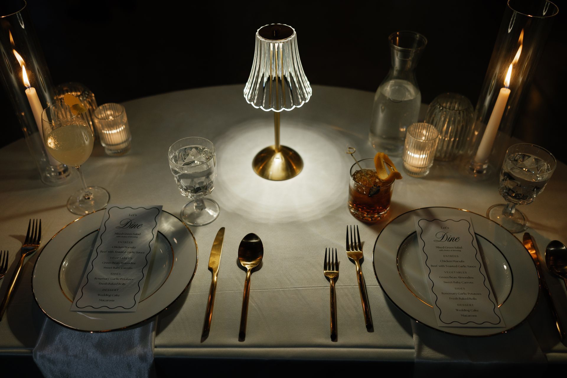 A table with plates , silverware , candles and a lamp on it
