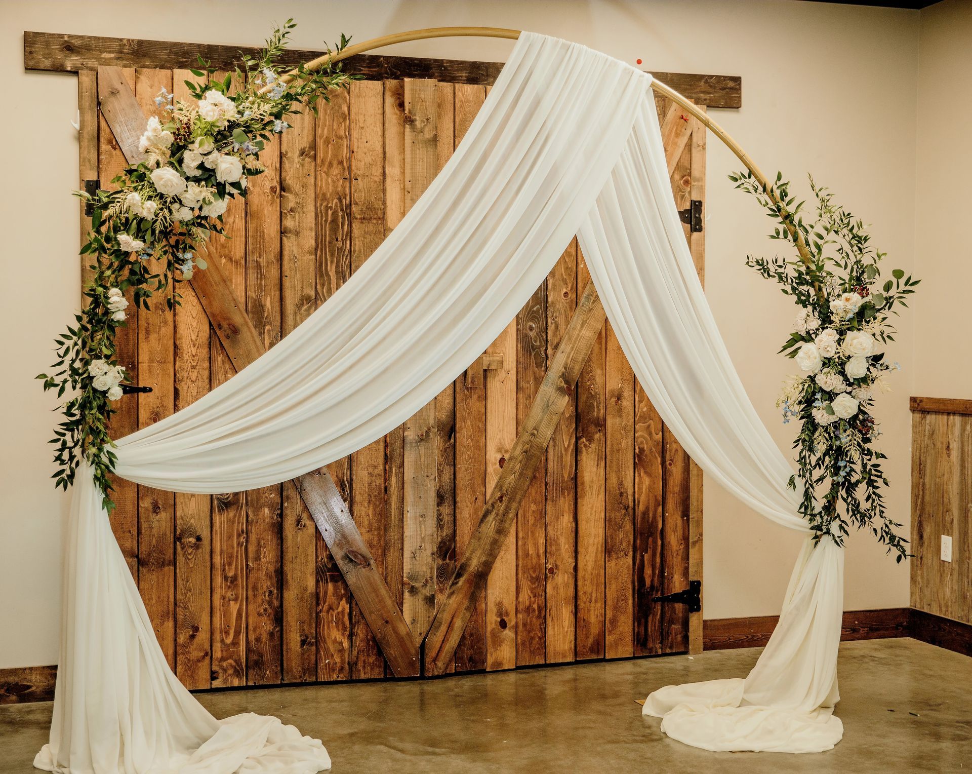 A wedding arch decorated with white flowers and greenery in front of a brick wall.