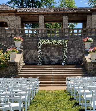 A row of white chairs are lined up in front of a stone building