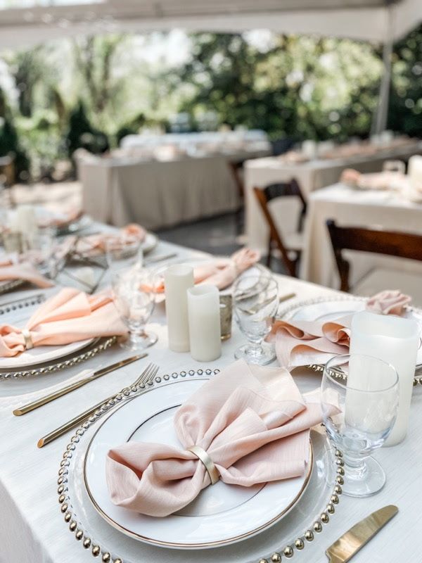 A table set for a wedding reception with plates , napkins , candles and glasses.
