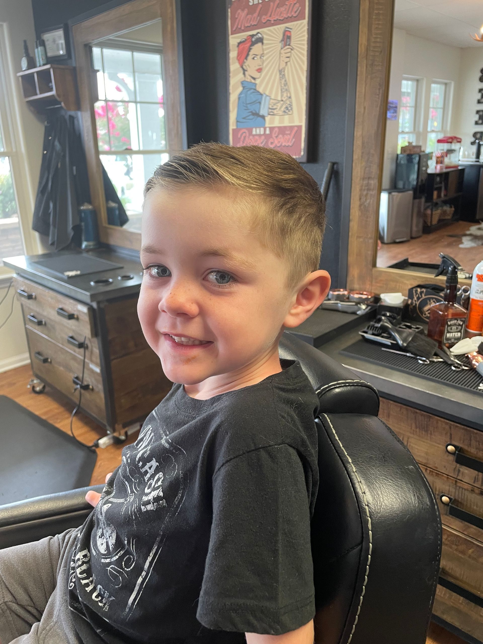 Smiling child in a barber chair with a fresh haircut; barber shop setting.