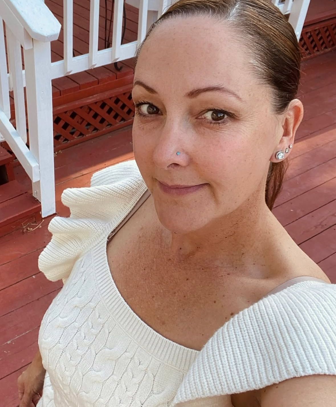 Woman in white sweater smiles on a wood deck.