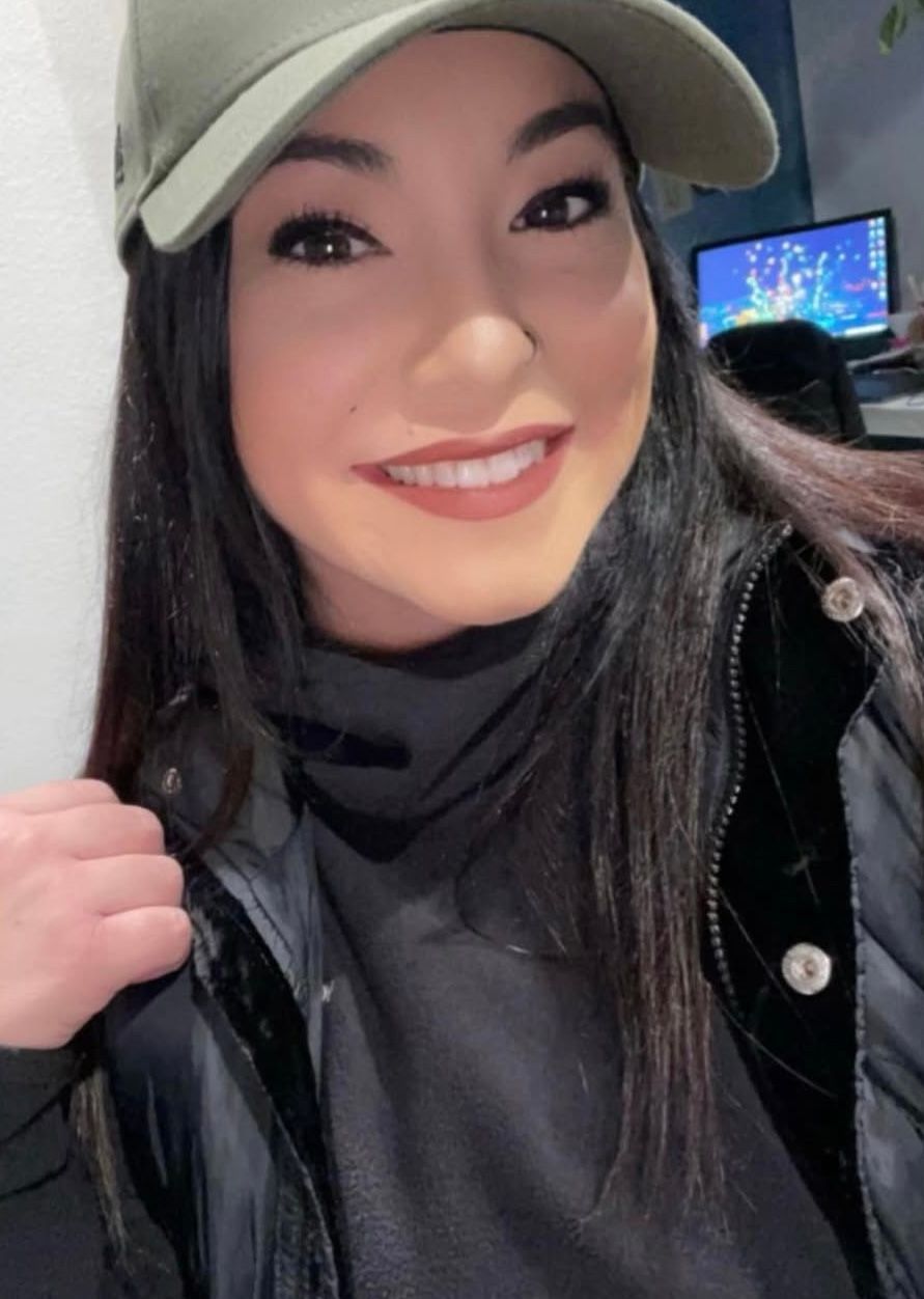 Woman wearing a green cap and black jacket, smiling at the camera.