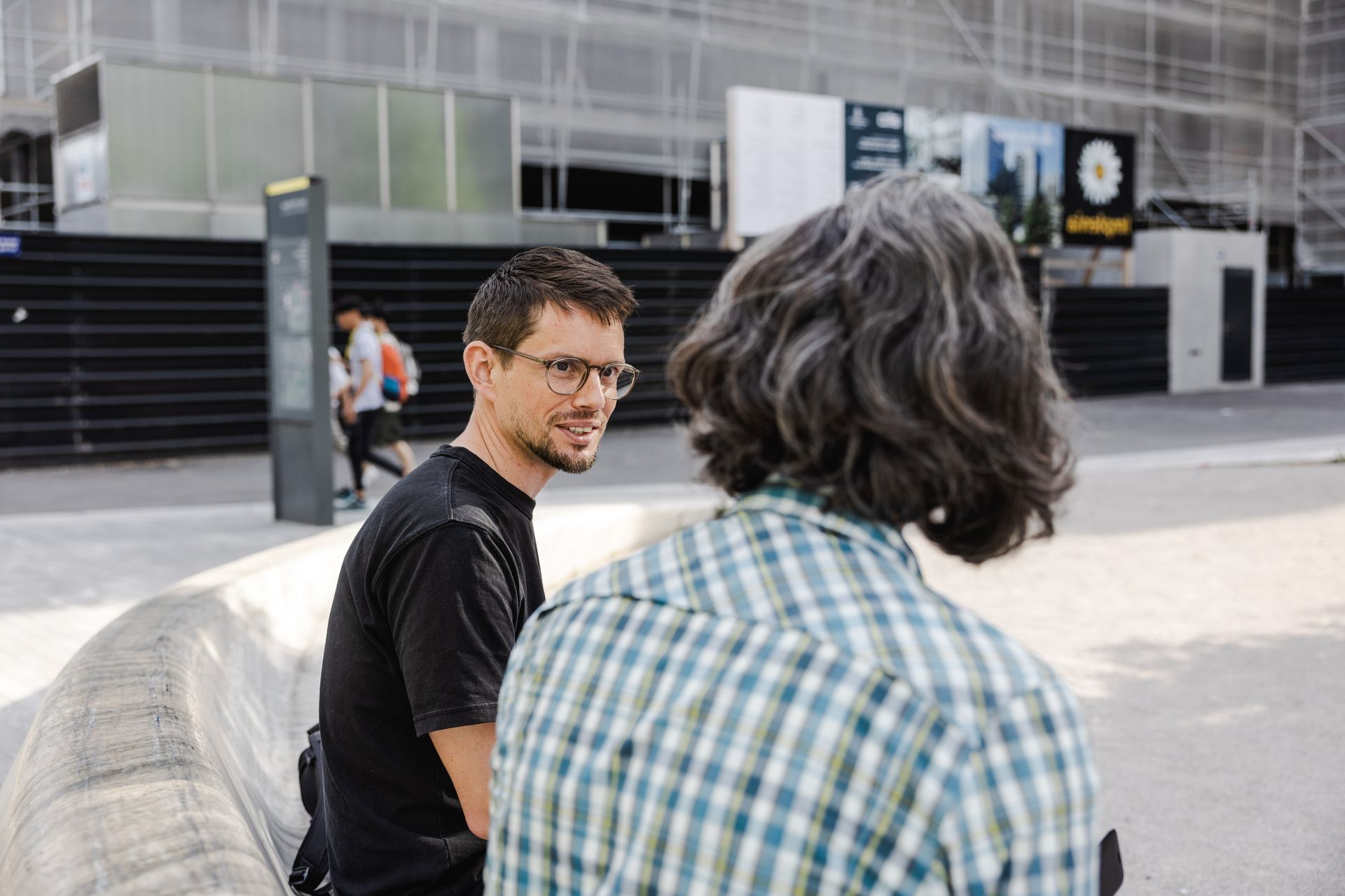 Deux personnes assises à des bureaux, utilisant des ordinateurs dans un environnement de bureau.
