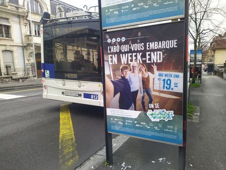 Un bus derrière un kiosque publicitaire bleu et blanc, dans une rue de la ville de Lausanne, avec une affiche promotionnelle pour l'abo weekend de Mobilis 
