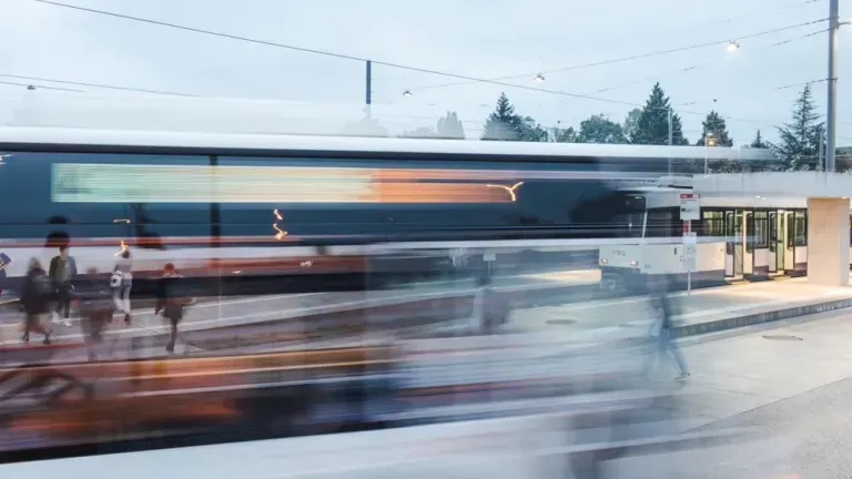 Vue floue d'un tram à une gare routière, des passagers qui marchent, ciel couvert.