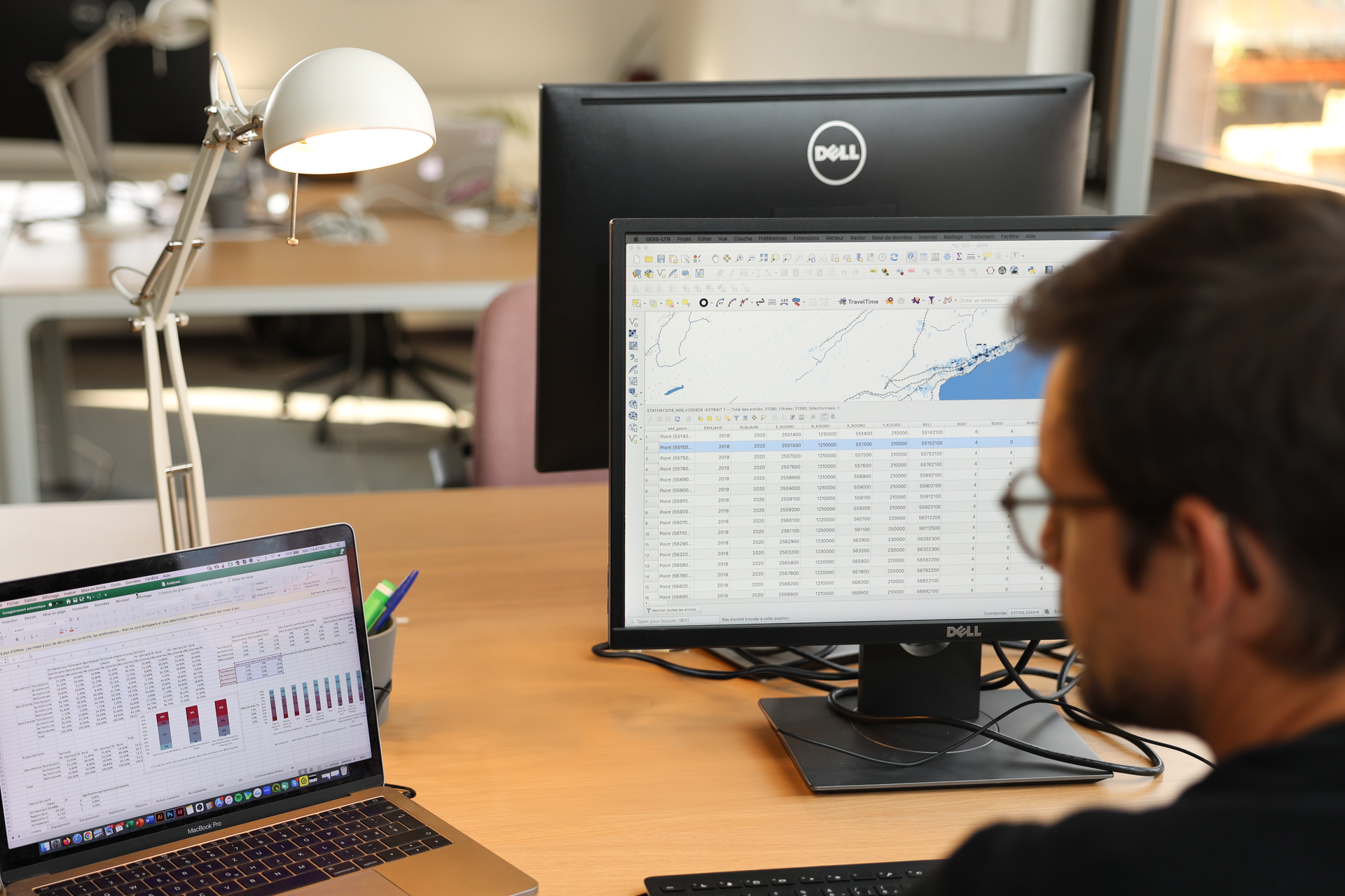 Un homme assis à son bureau consulte des feuilles de calcul sur son ordinateur portable et son écran d'ordinateur au bureau.