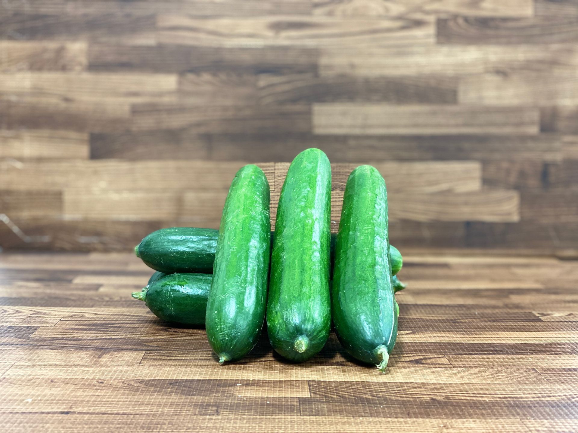 Several green cucumbers on a wooden surface, with a wood-grain background.