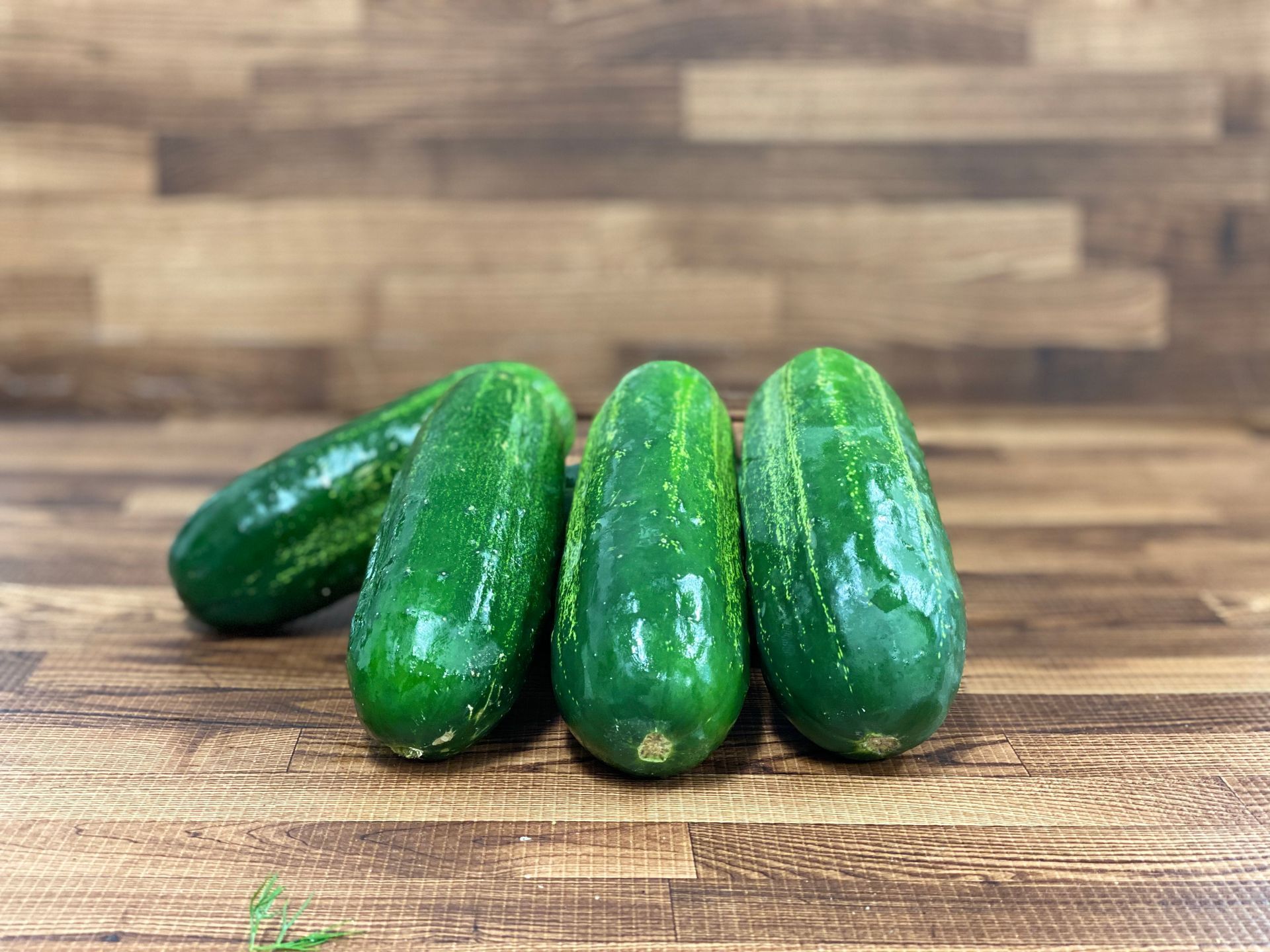 Four green cucumbers on a brown wooden surface.