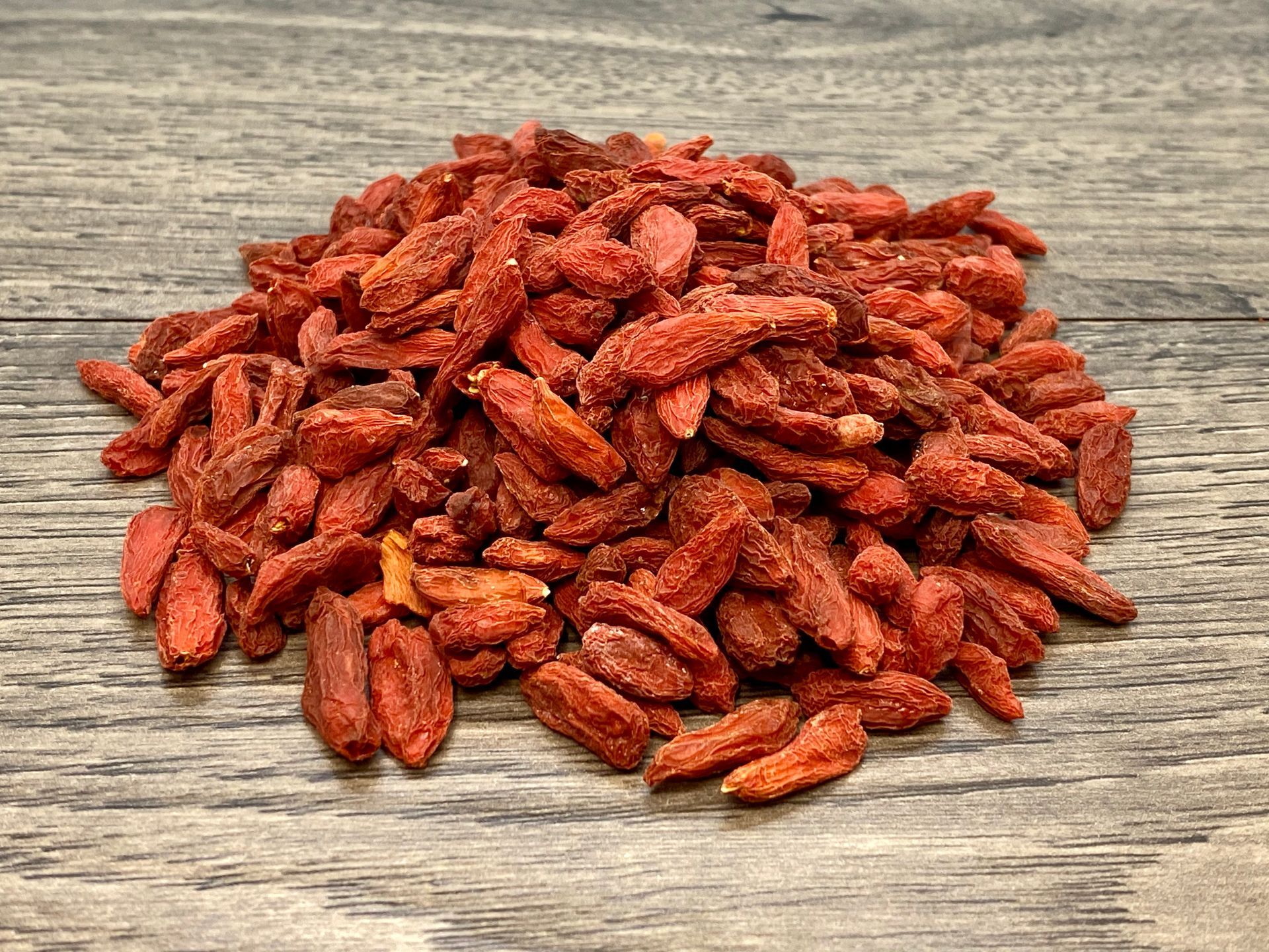 Pile of dried, reddish-orange goji berries on a wooden surface.