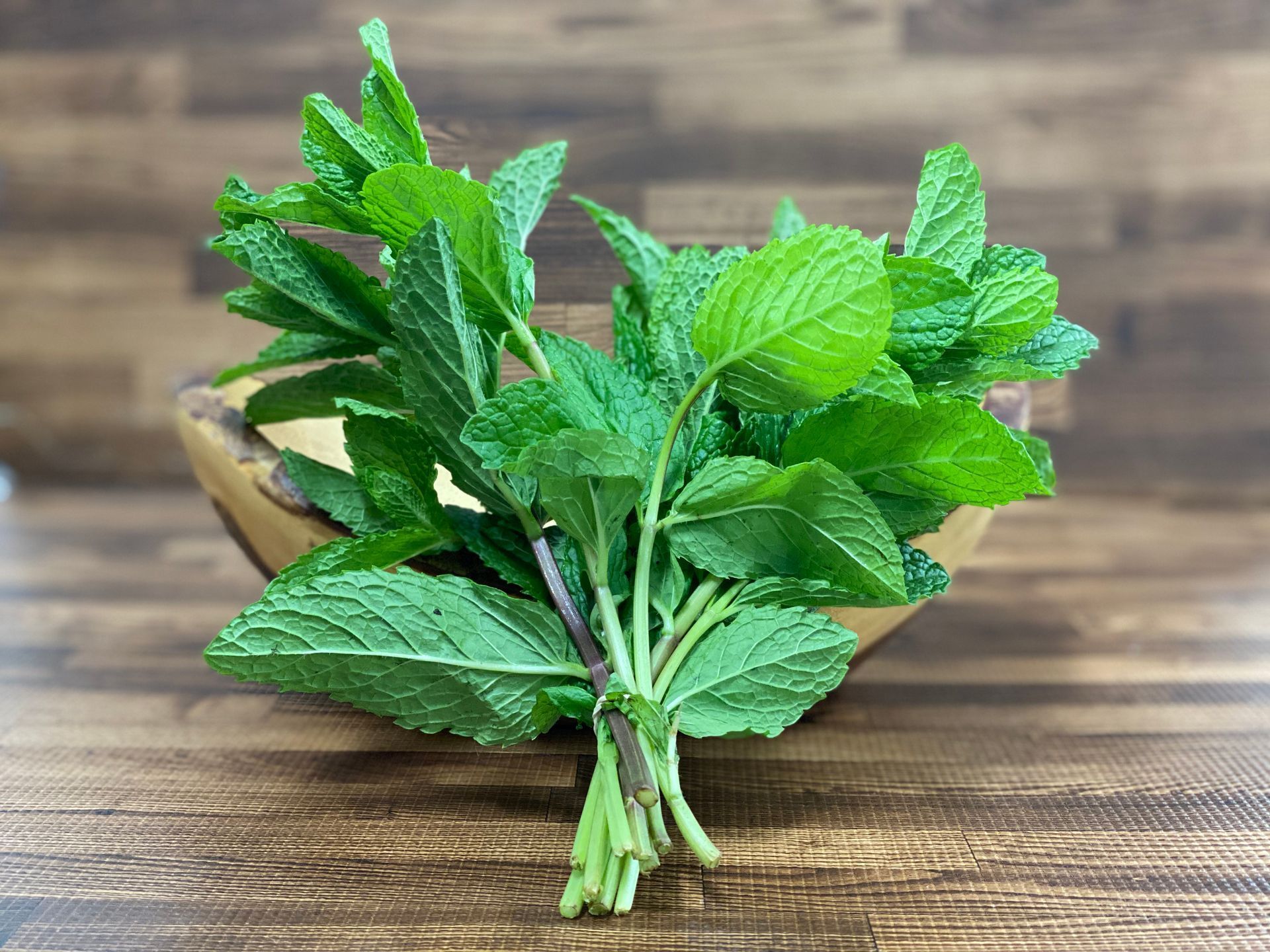 Bundle of fresh green mint leaves in a wooden bowl on a wood surface.