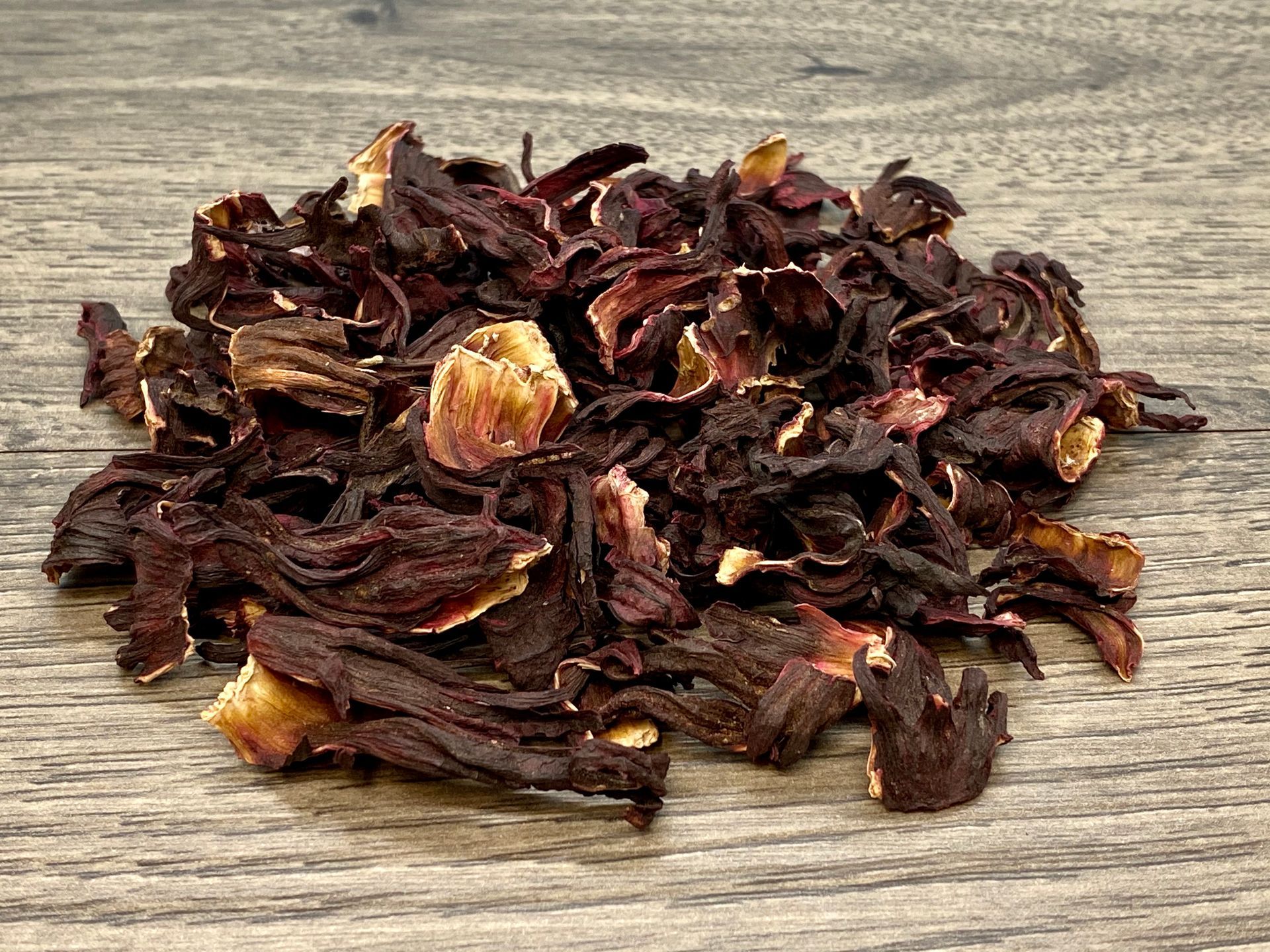 Dried hibiscus flowers on a wood surface, deep red and brown hues.
