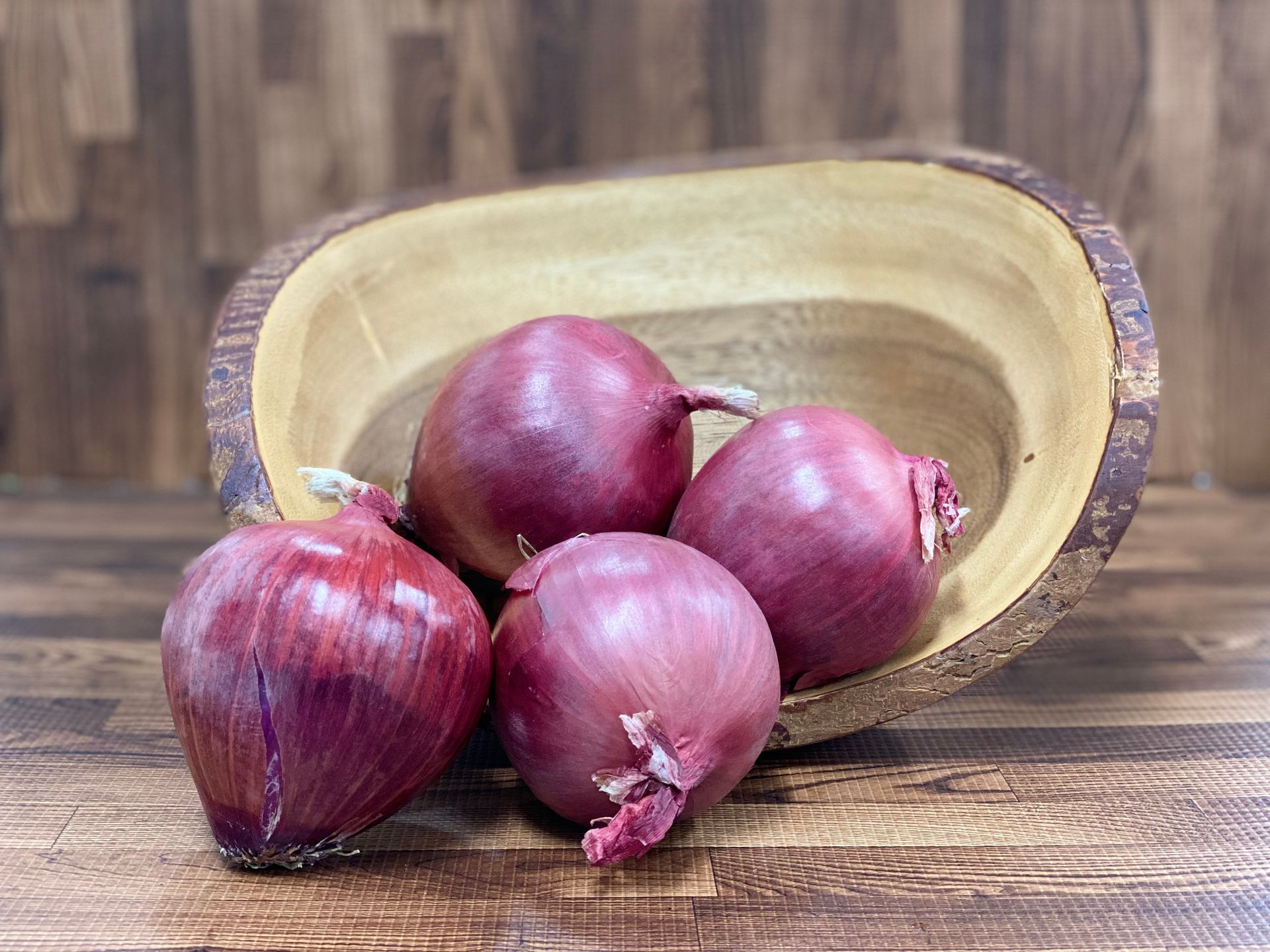 Four red onions in and around a wooden bowl, set on a wooden surface.