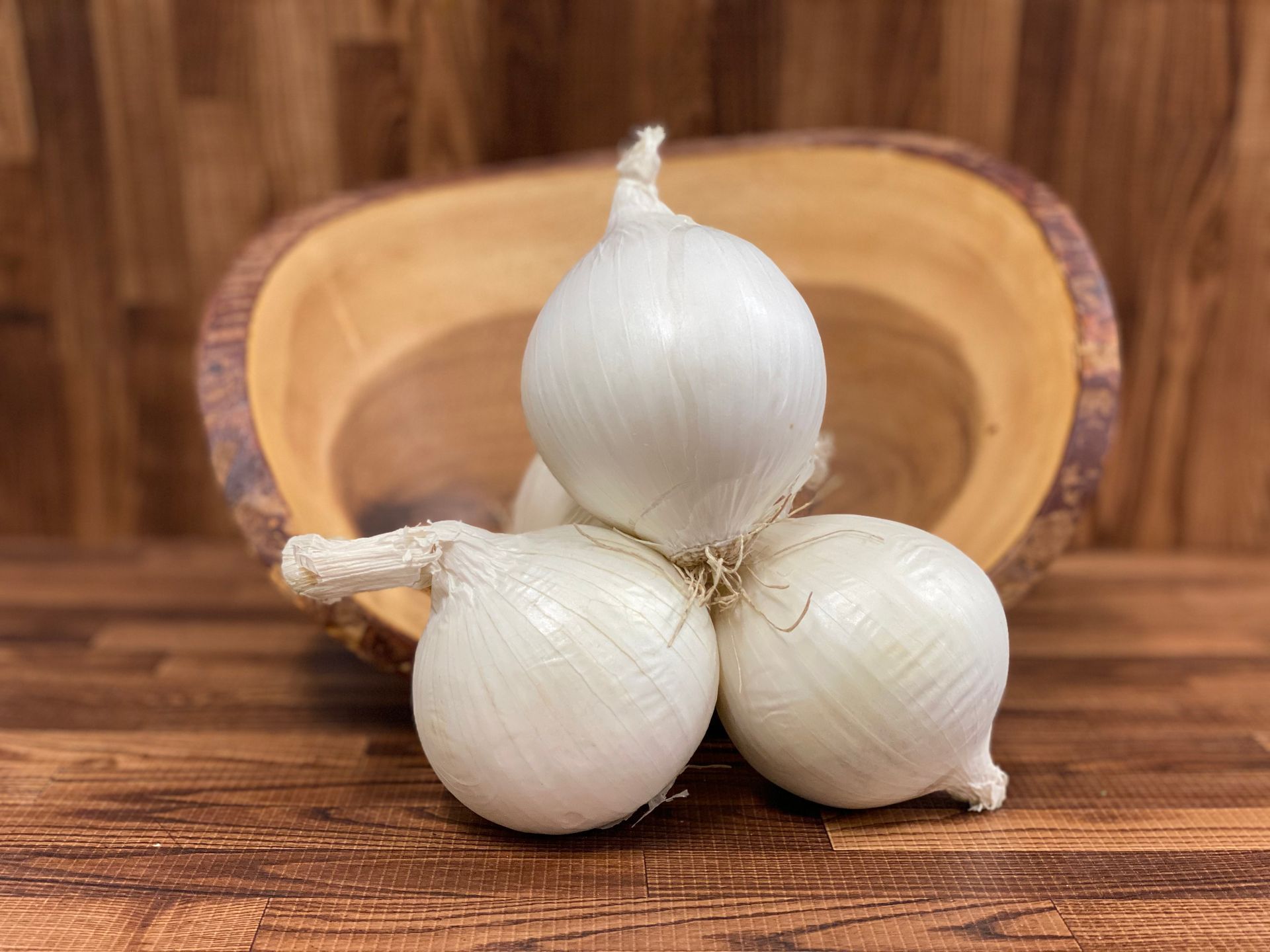 White onions sit on a wooden surface next to a wooden bowl.