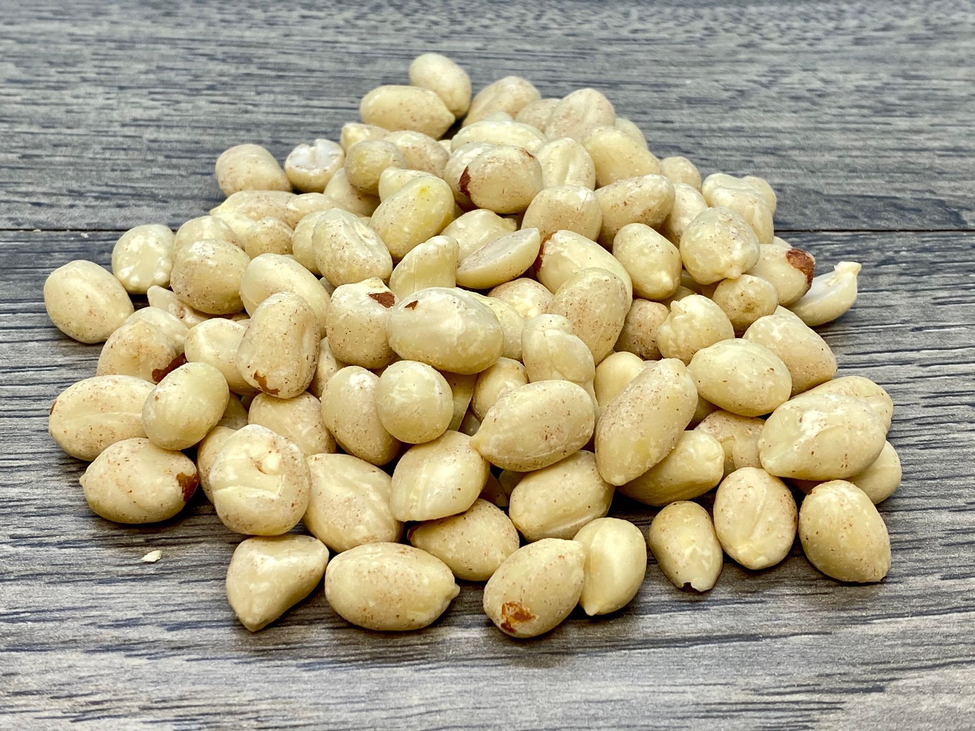 Pile of blanched peanuts on a gray wood surface.
