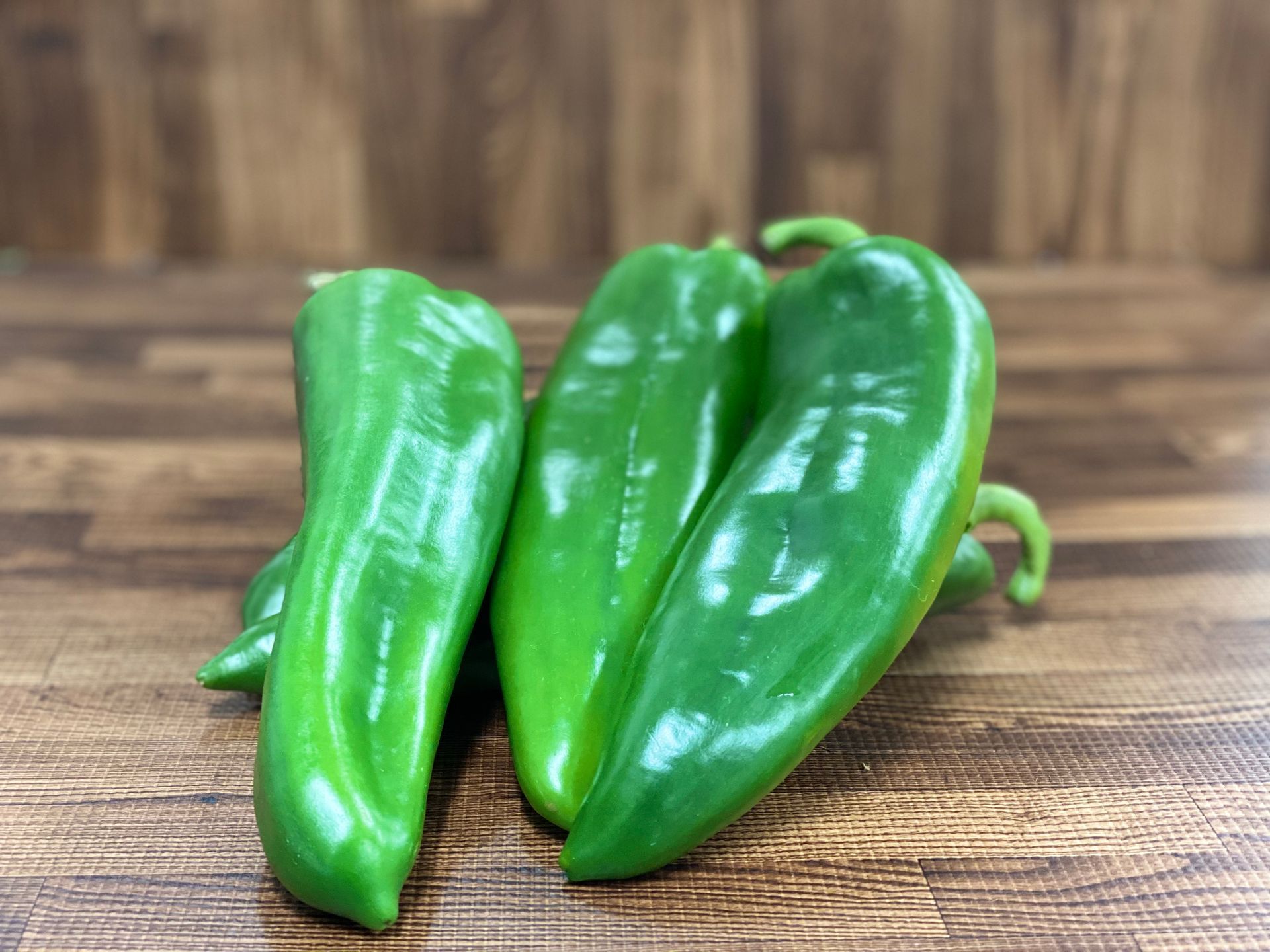 Green Anaheim peppers on a wooden surface.