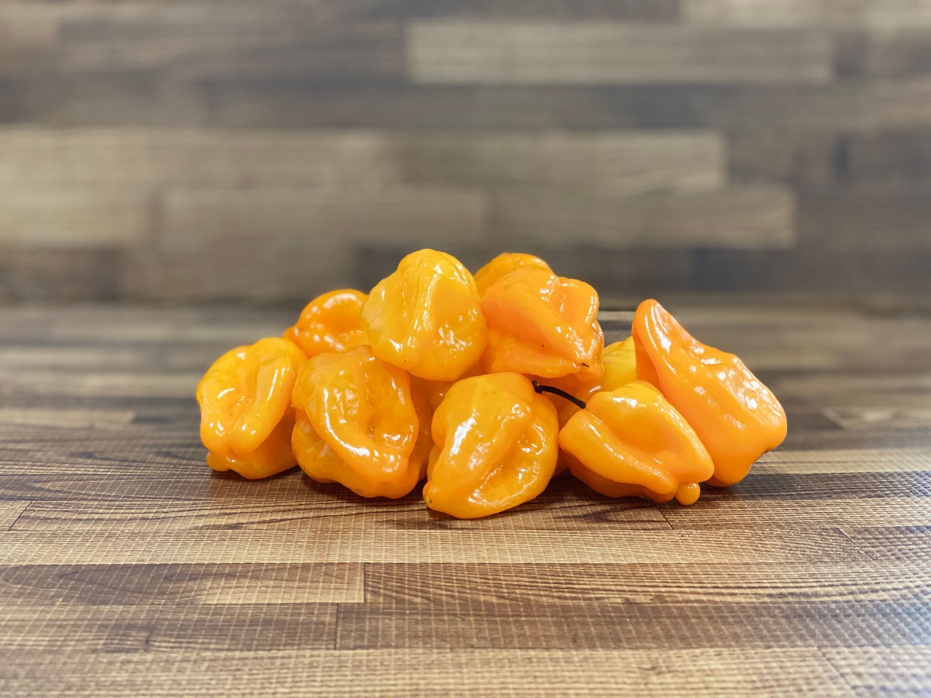 Yellow habanero peppers piled on a wooden surface.