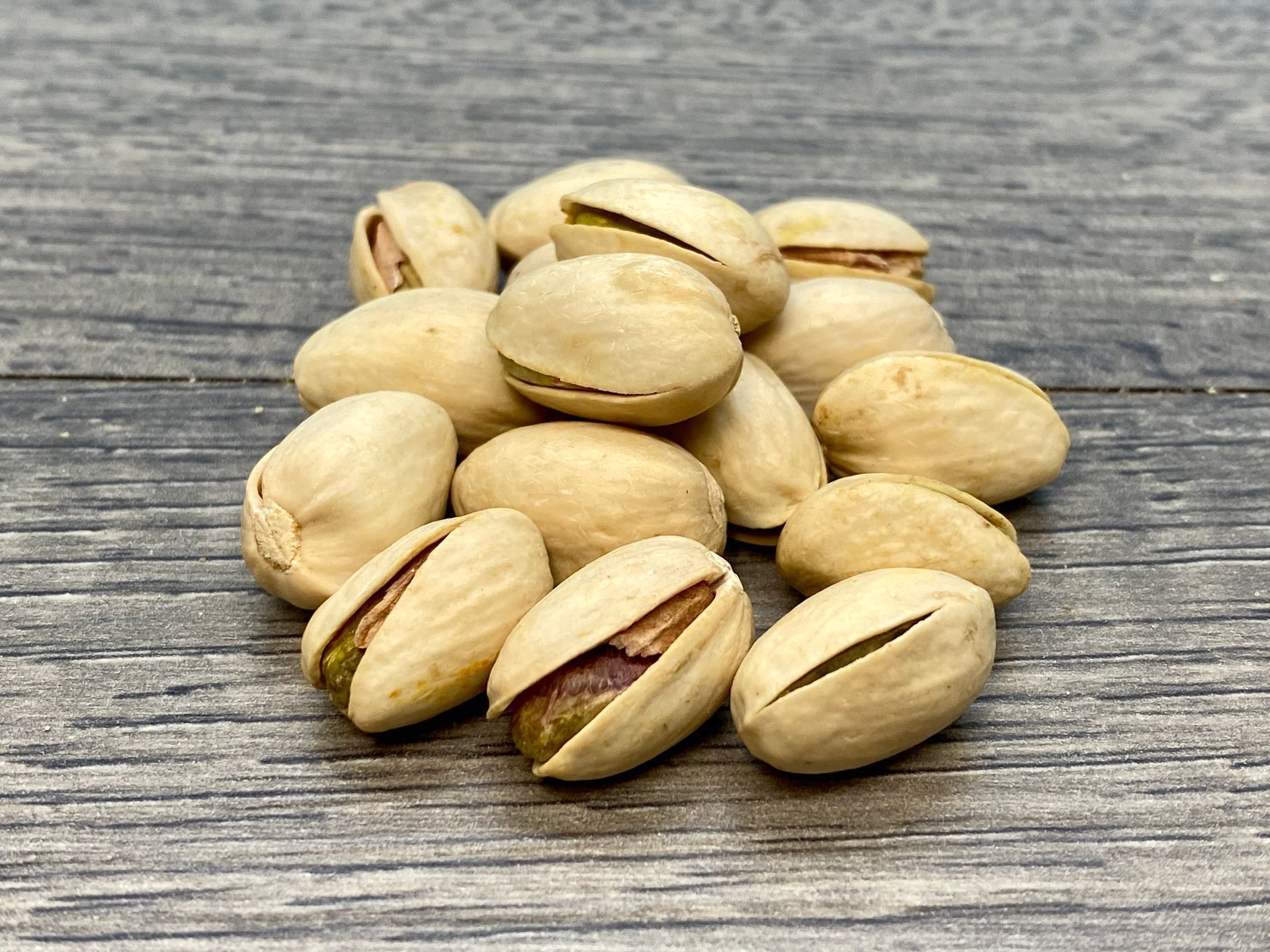 Pile of shelled pistachios on a grey wooden surface.