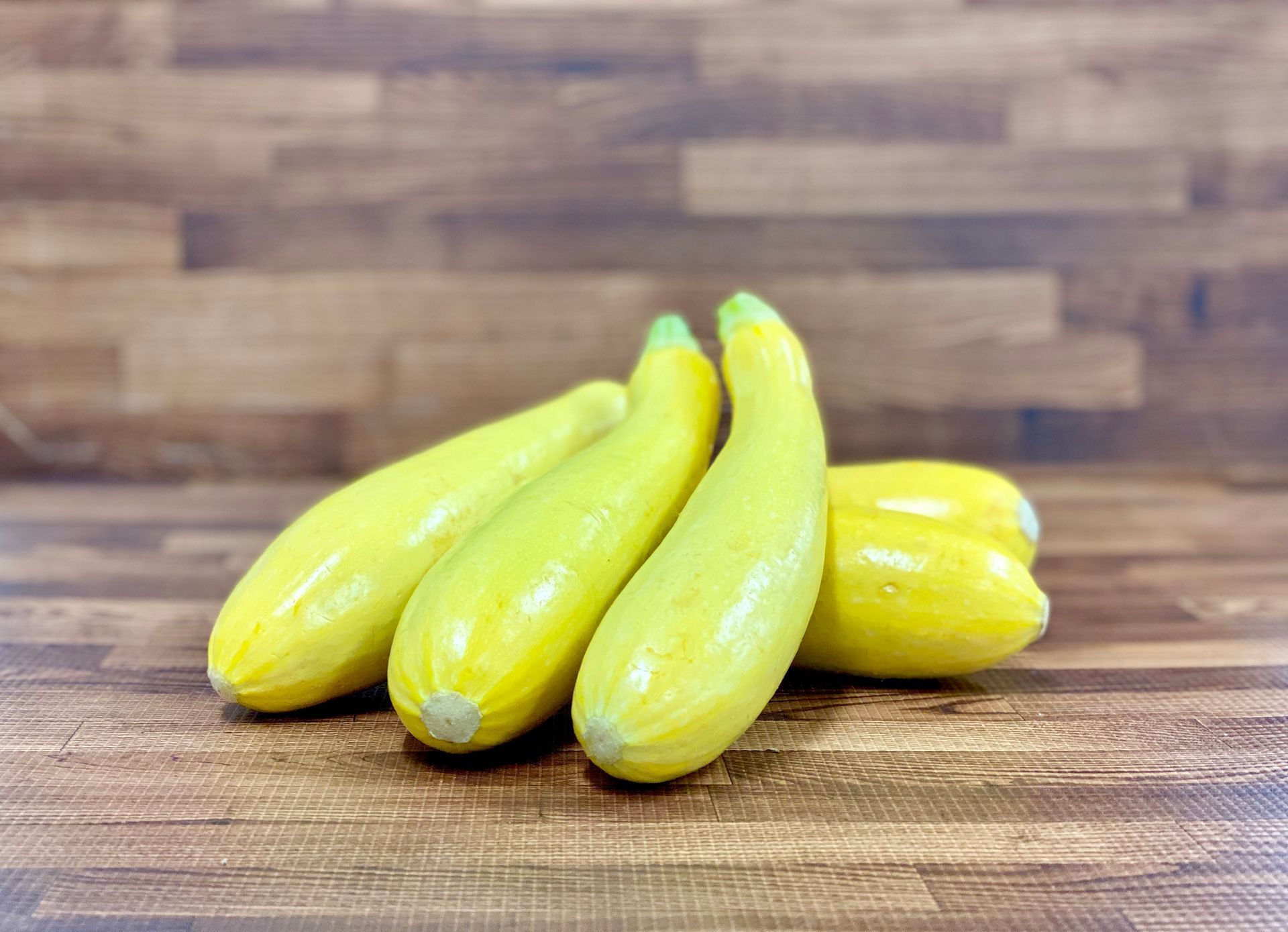 Four yellow squash on a wooden surface.
