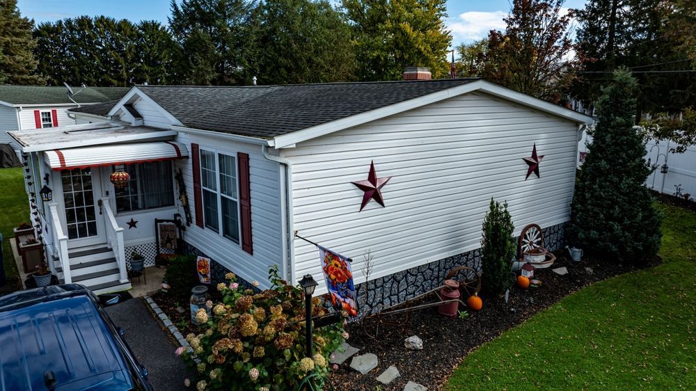 White house with red star decorations, flower beds, and a small porch surrounded by greenery