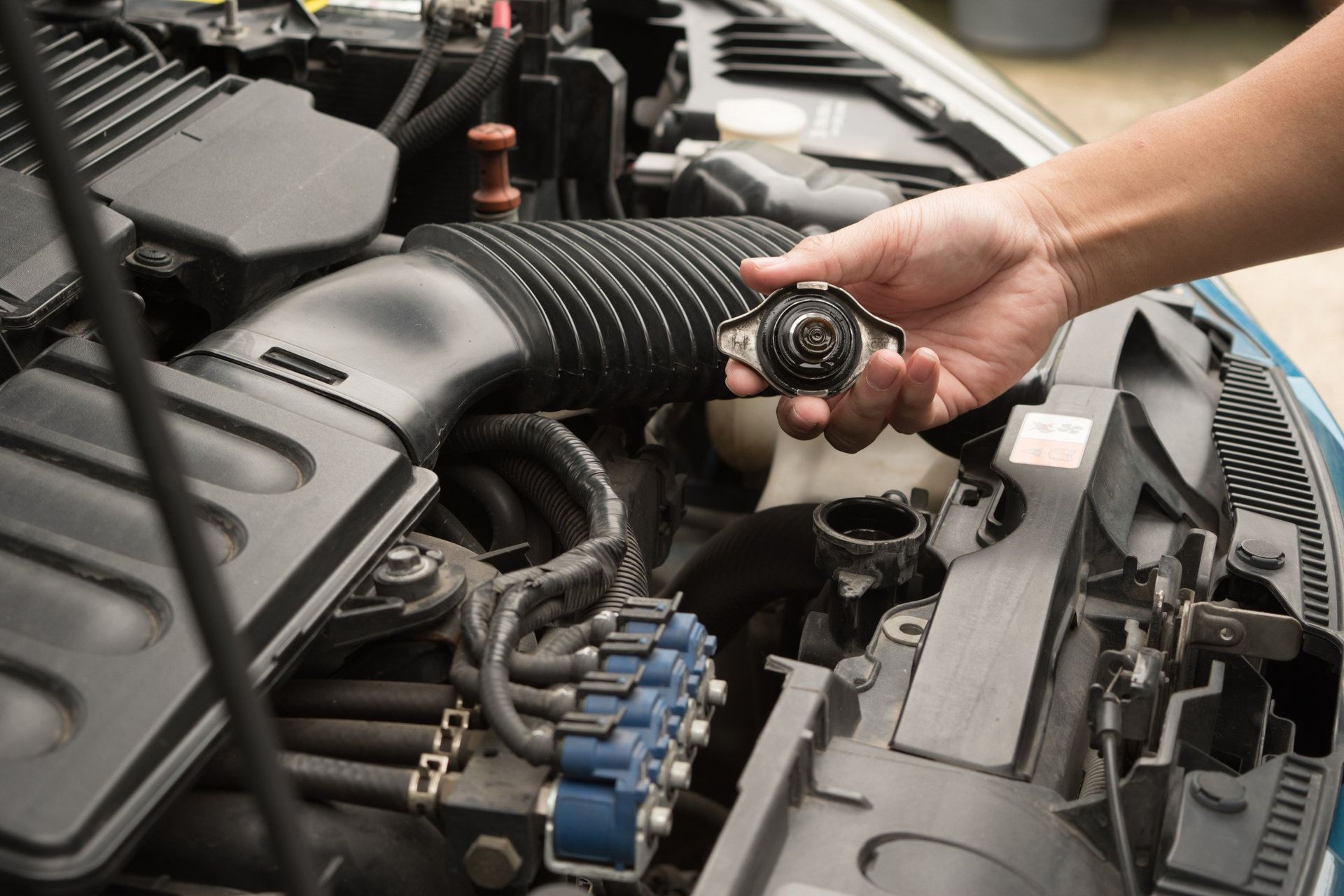 A person is holding a radiator cap under the hood of a car.