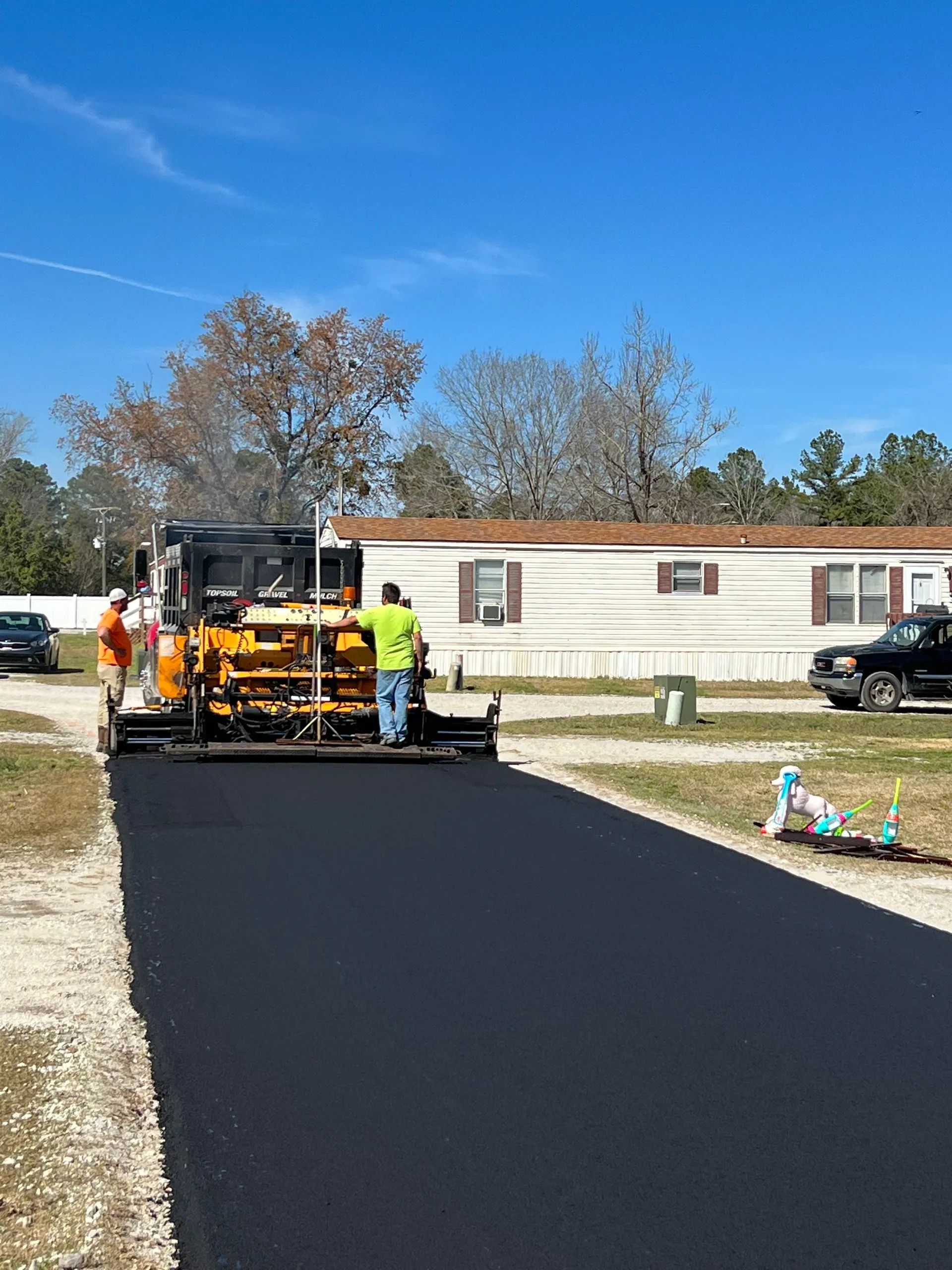 Asphalt paving machine laying blacktop on a residential road. Workers in safety vests.