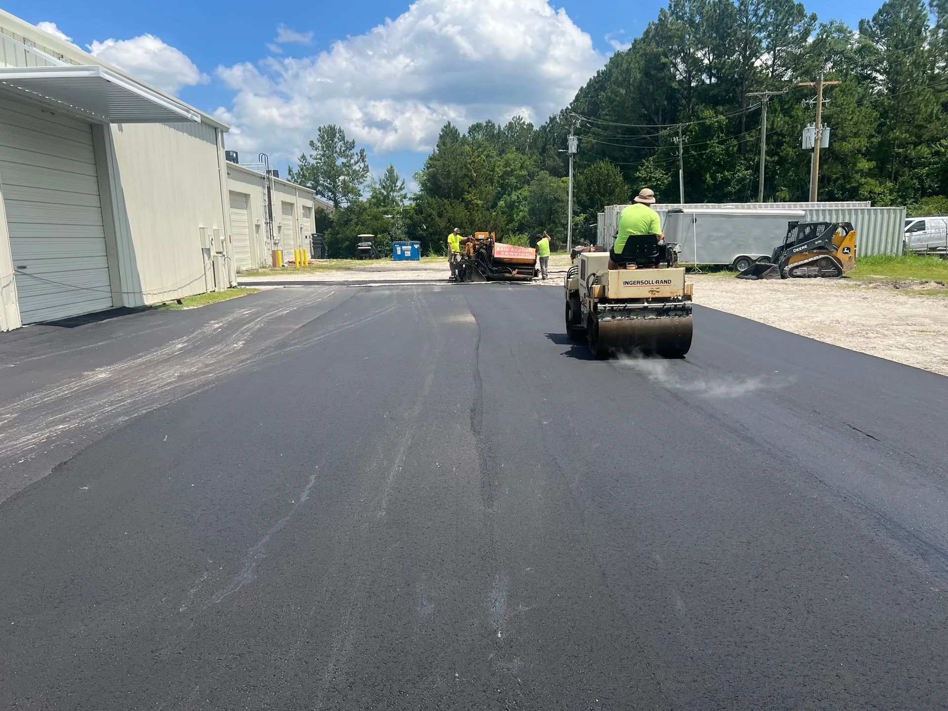 Asphalt paving with a roller flattening the fresh black surface.