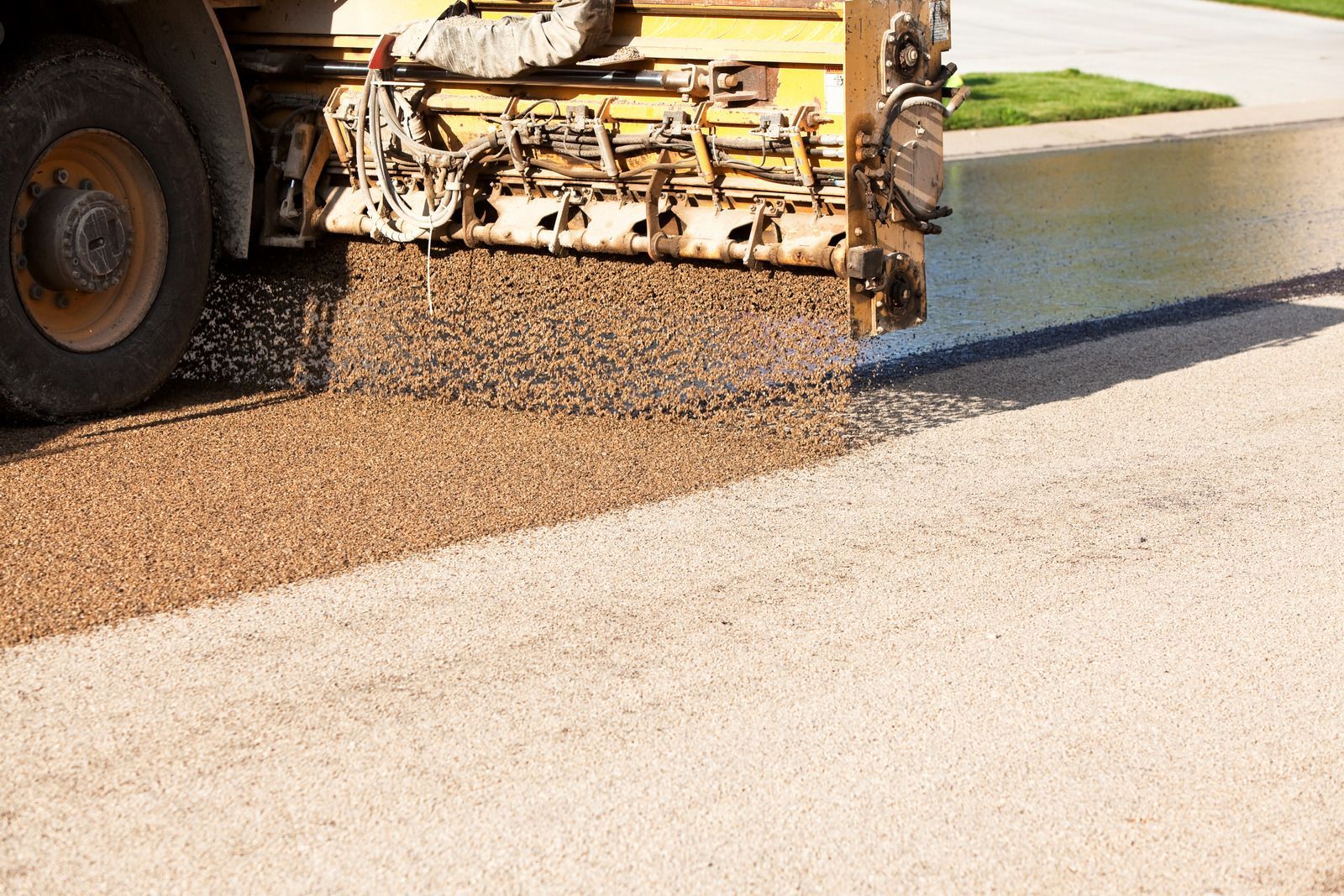 Roadwork: Truck applying gravel to asphalt road.