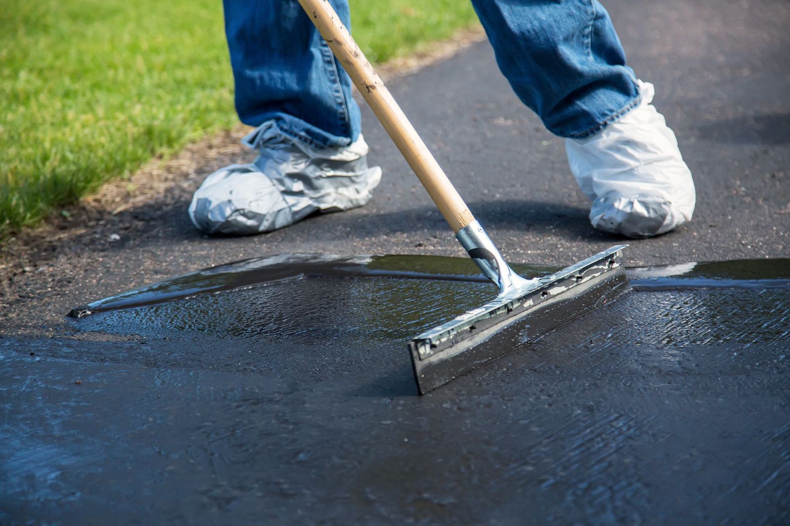 A person is using a squeegee to spread asphalt on a driveway.