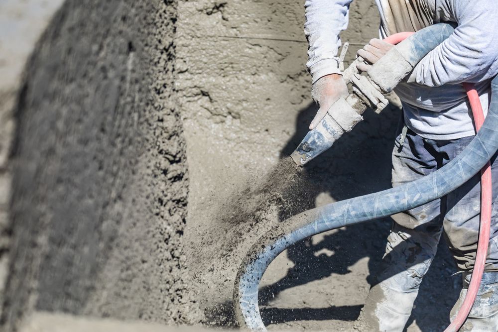 Person Spraying Concrete Onto a Wall With a Hose, Outdoors — Nambucca Concrete Pumping in Nambucca Heads, NSW