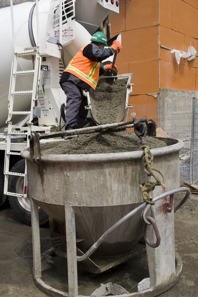 Worker in Orange Vest Pours Concrete From a Truck Into a Large Container — Nambucca Concrete Pumping in Grafton, NSW