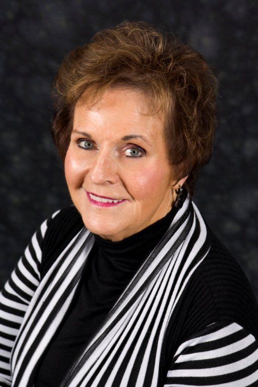 Woman with brown hair smiles, wearing black turtleneck and black/white striped cardigan.