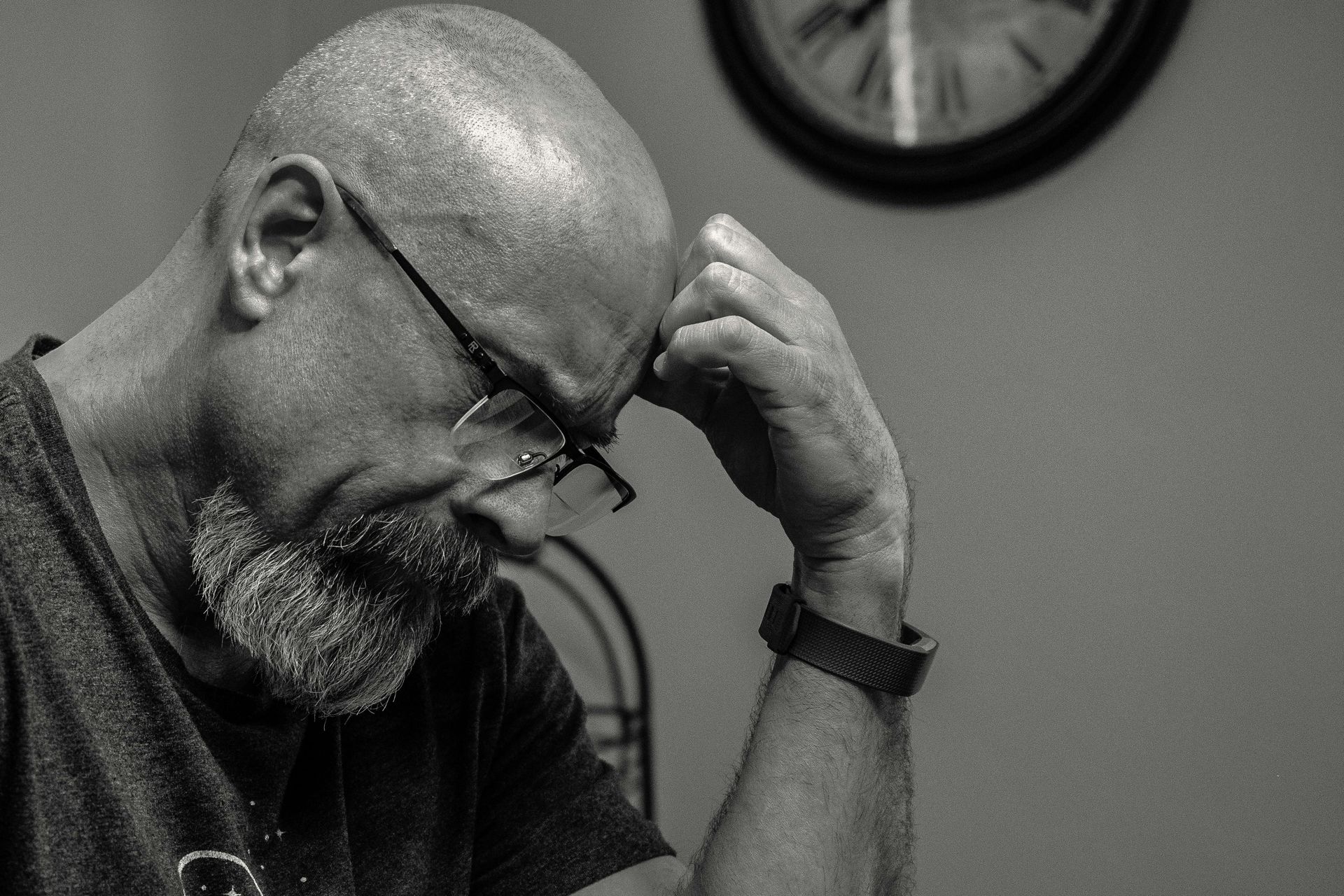 A man with glasses and a beard is sitting in front of a clock
