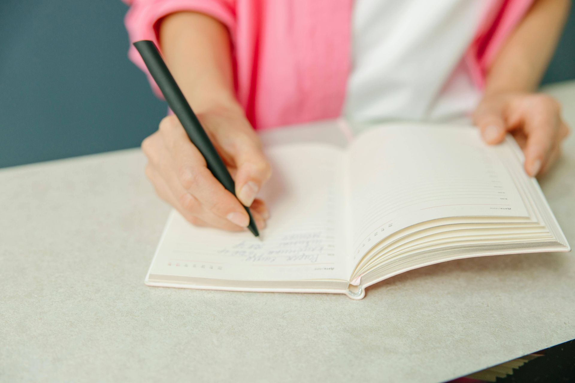 A woman is writing in a notebook with a pen.