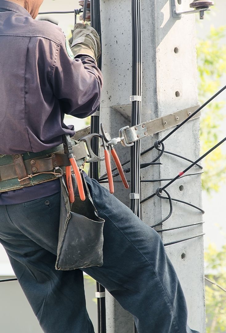 A man is working on a power pole with a pair of pliers.