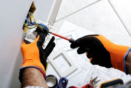 An electrician is working on a light switch with a screwdriver.