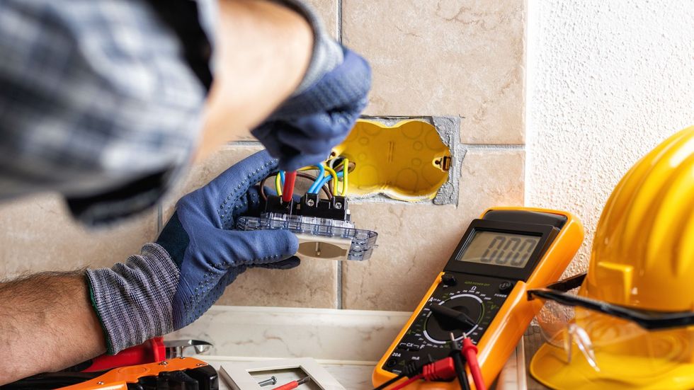 An electrician is working on an electrical outlet on a wall.