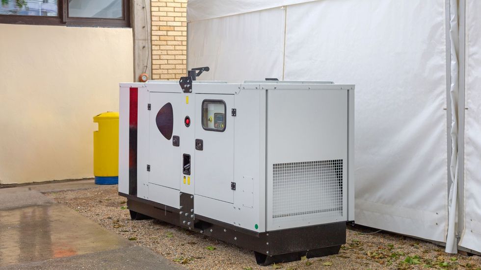 A generator is sitting outside of a building next to a tent.